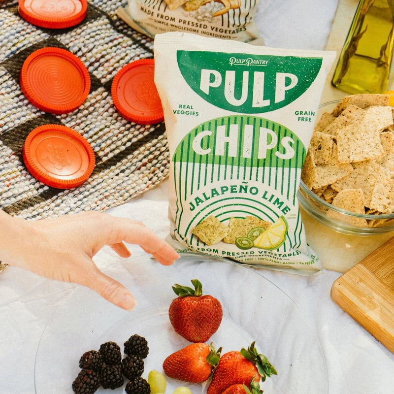 A variety of foods laid out on a picnic blanket including a bag that reads