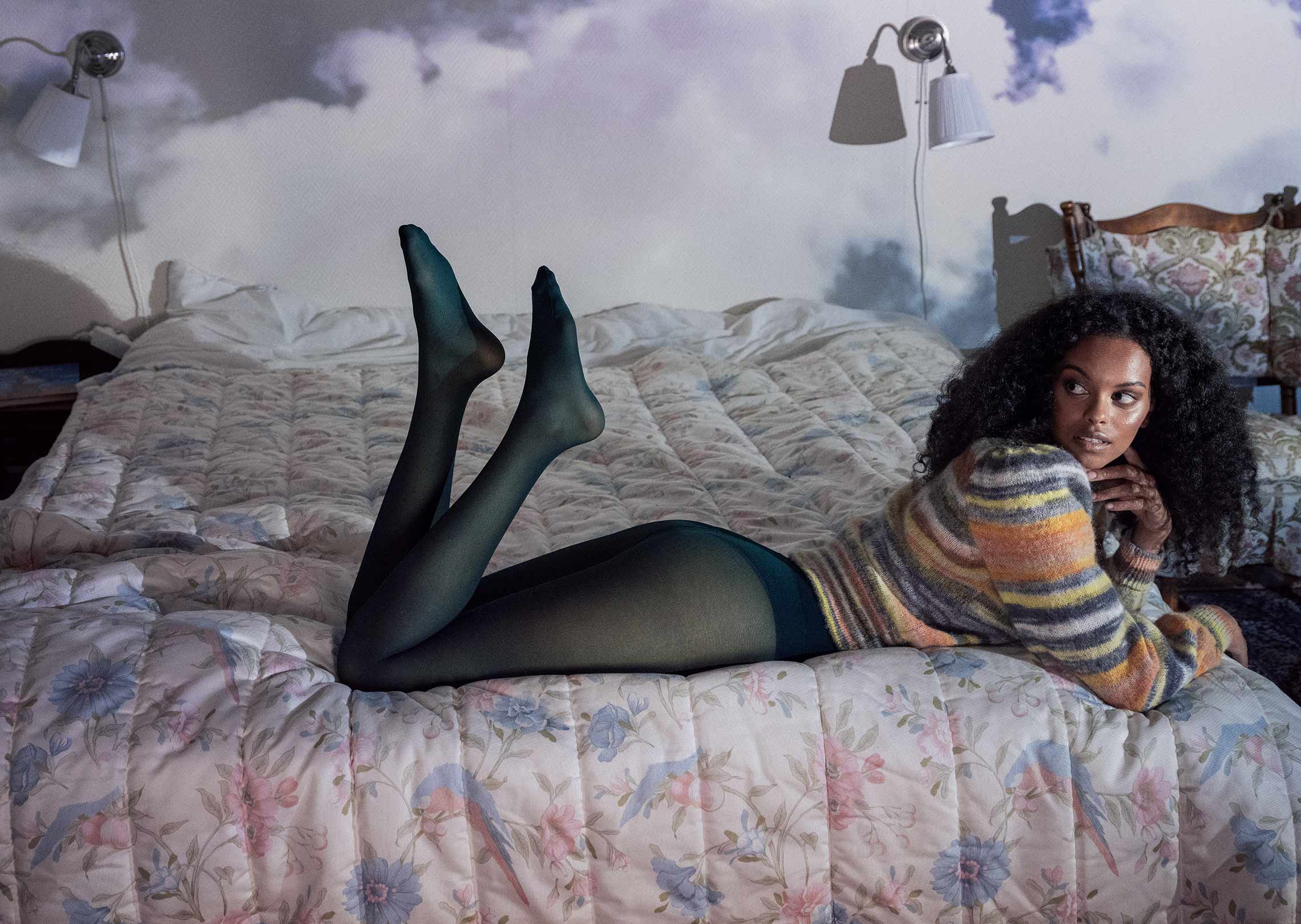 A person wearing tights lounges on a floral bed