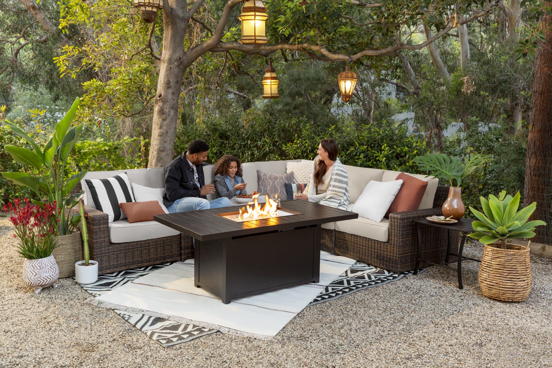 A family sits on patio furniture in a lush backyard