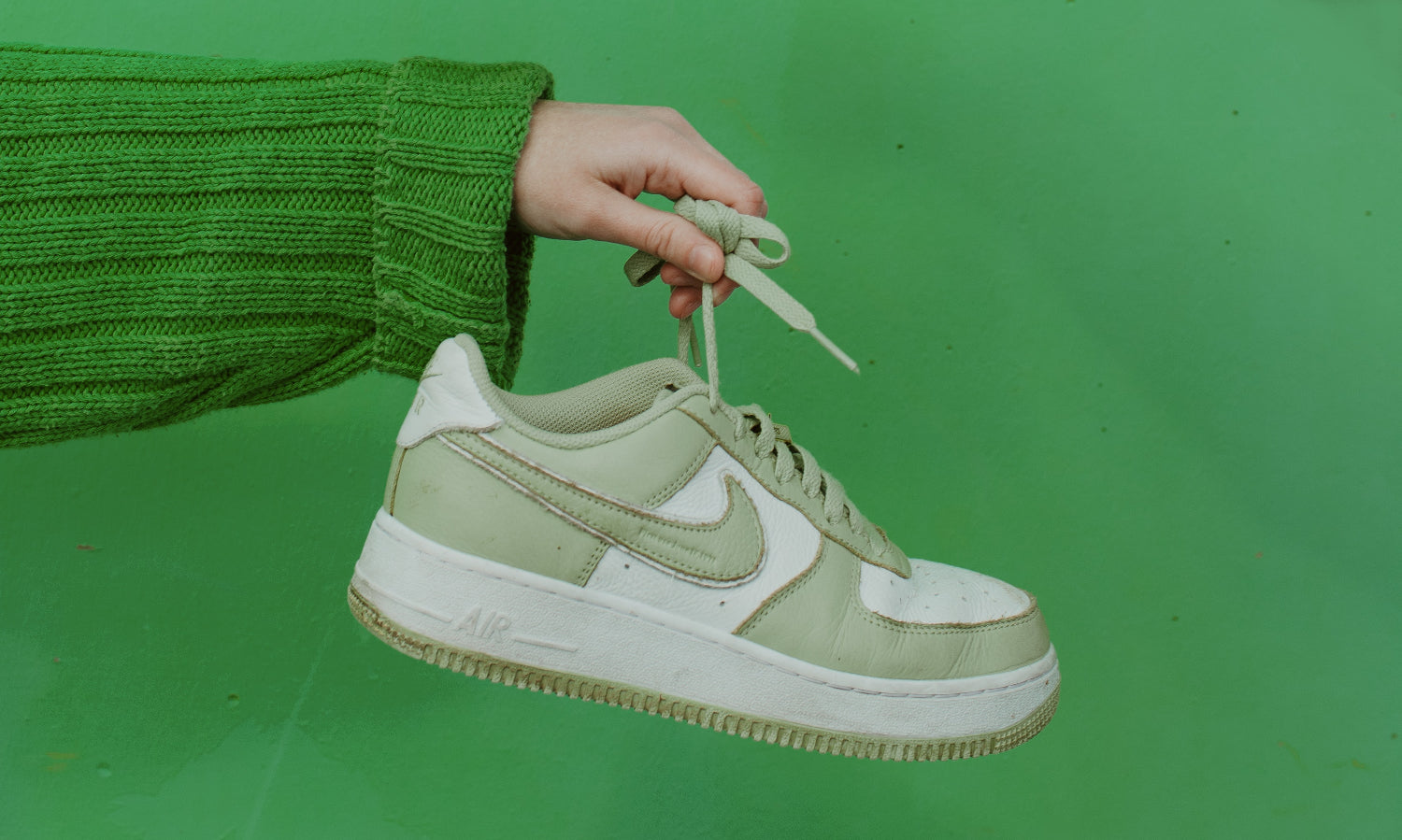 一个人在绿色的背景前拿着一只绿色的运动鞋