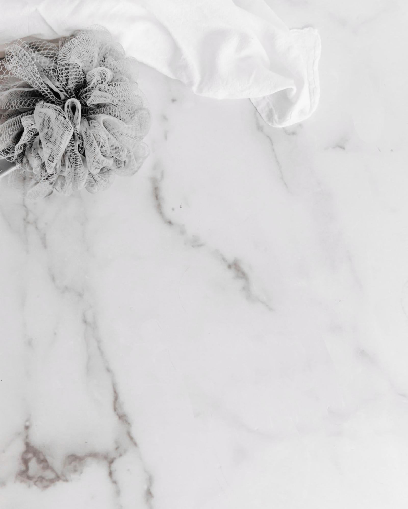 overhead shot of marble surface with grey luffa and white hand towel in top left corner