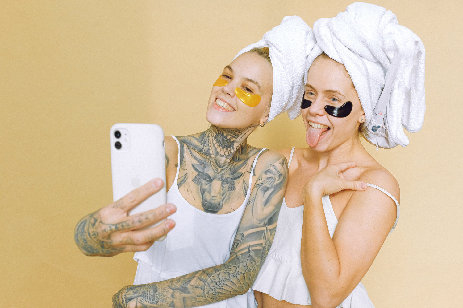 Two people wearing towels on their heads and spa eyemasks take a selfie
