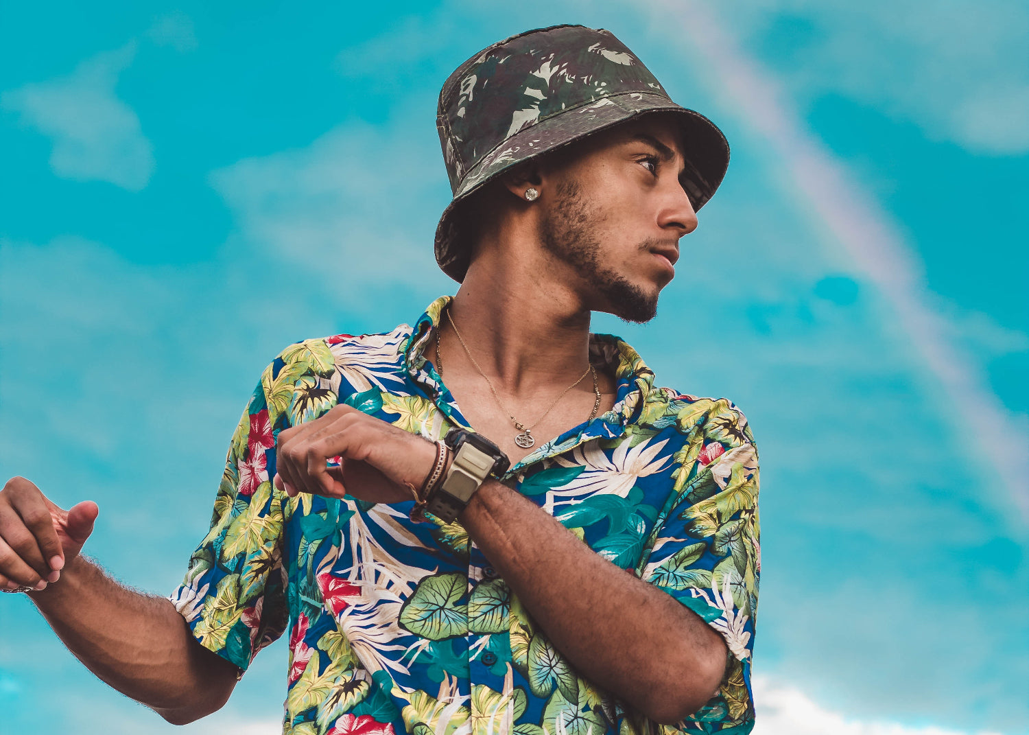 A young man in a bucket hat and patterned shirt dances outside