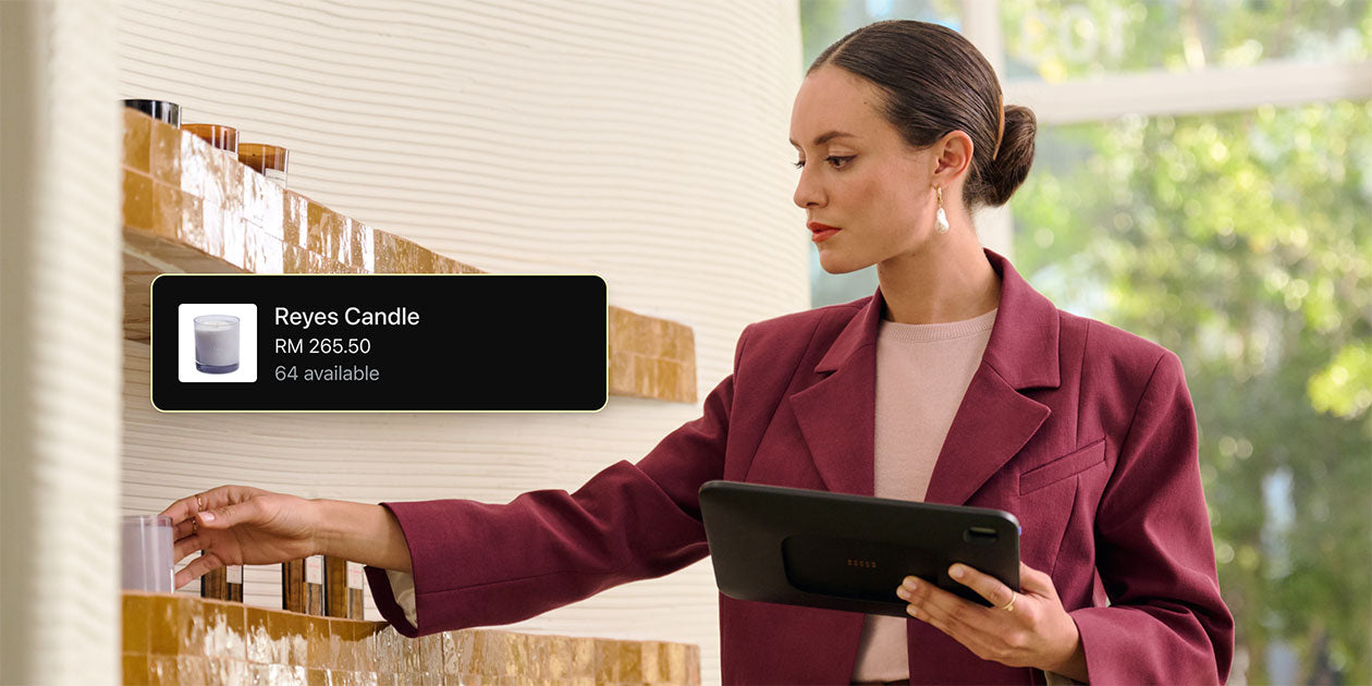 A sales associate on the sales floor reaches for a product while also holding a tablet running Shopify POS. Over the image is a screen from Shopify POS showing the product, its price, and how many are in stock.